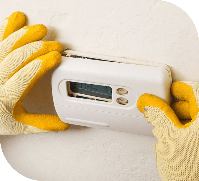 A person wearing yellow gloves is adjusting the thermostat.