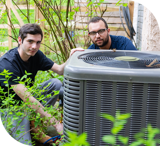 Two men are sitting next to a large air conditioner.